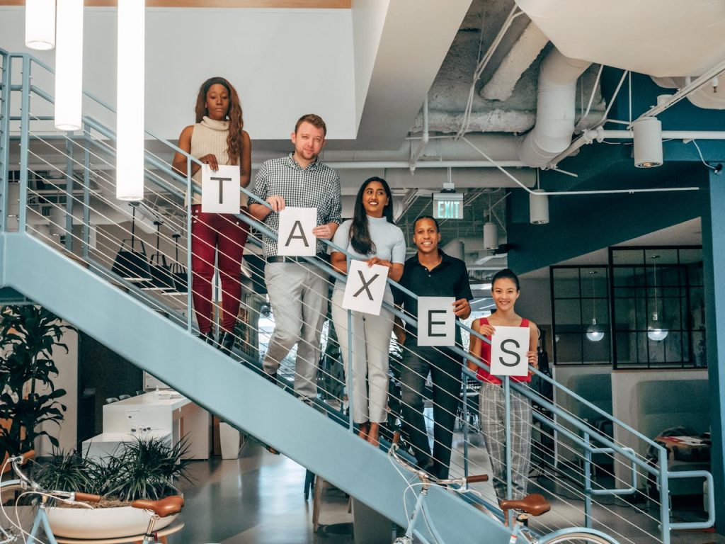 Multicultural business team holding Taxes signs on a modern office staircase, symbolizing collaboration.